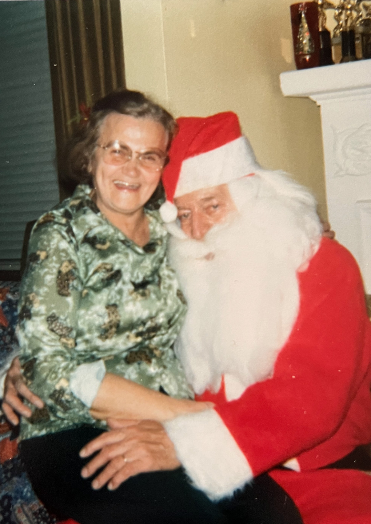 A smiling woman sitting with a man dressed up as Santa.