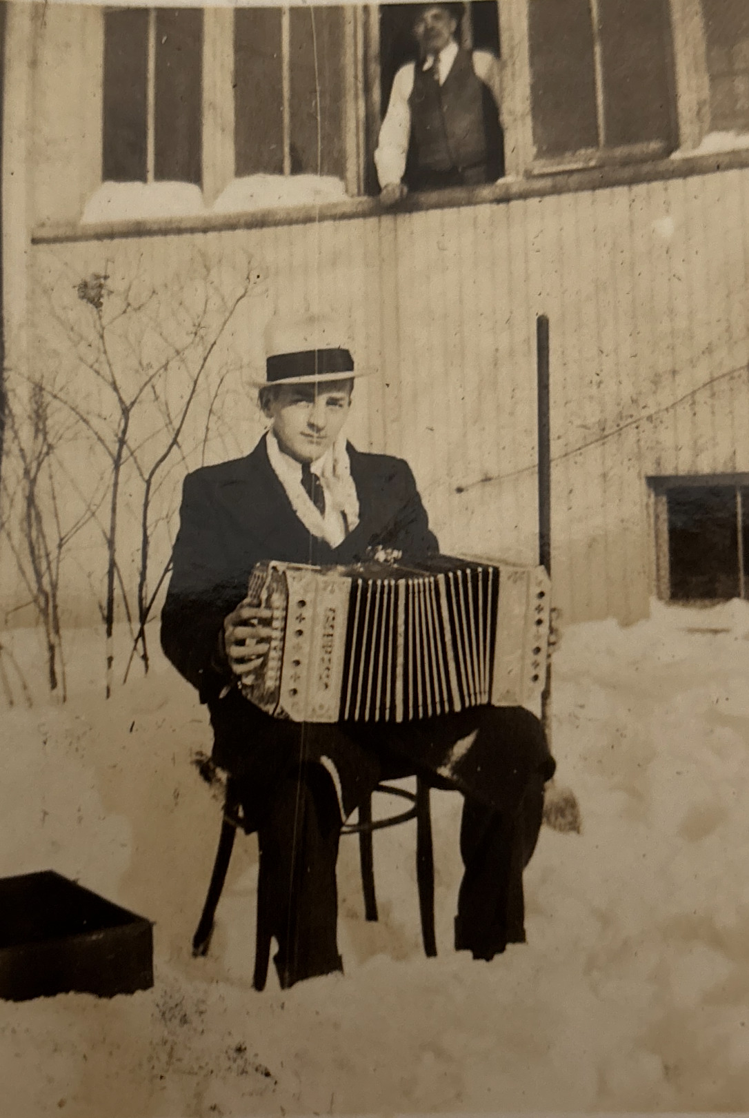 (Black and white) A sharply-dressed man sitting in snow holding a concertina.